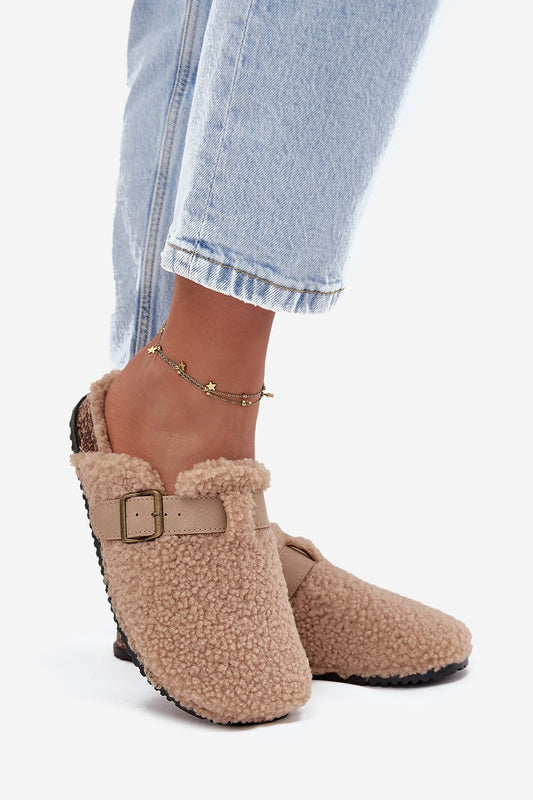 Beige slippers with fur trim worn with light blue jeans on a white background