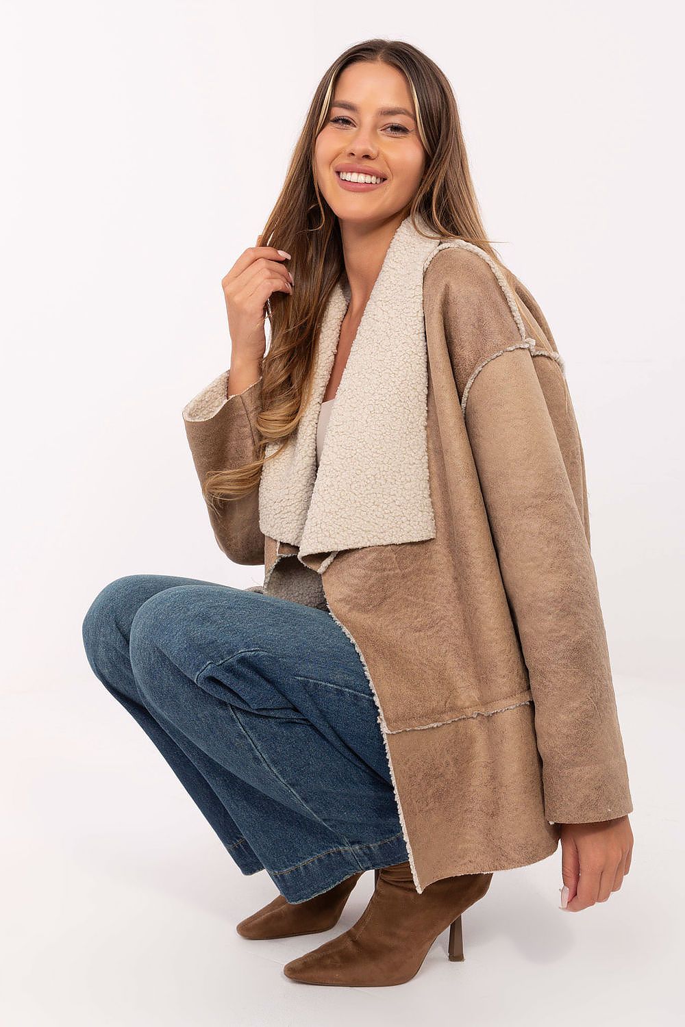 Woman wearing a brown coat with a white shirt and blue jeans on a white background