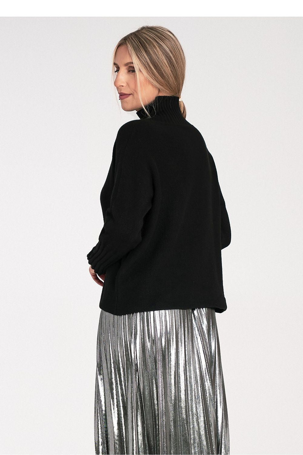 Woman wearing a black turtleneck and silver pleated skirt on a white background