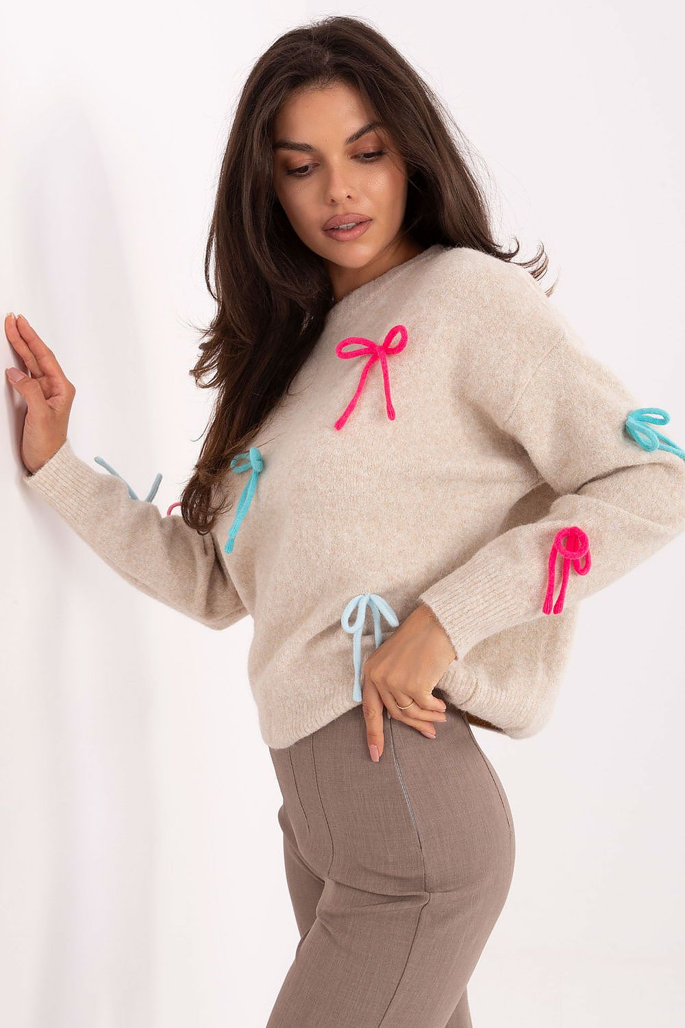Beige bow-accented sweater paired with jeans, casual styling.