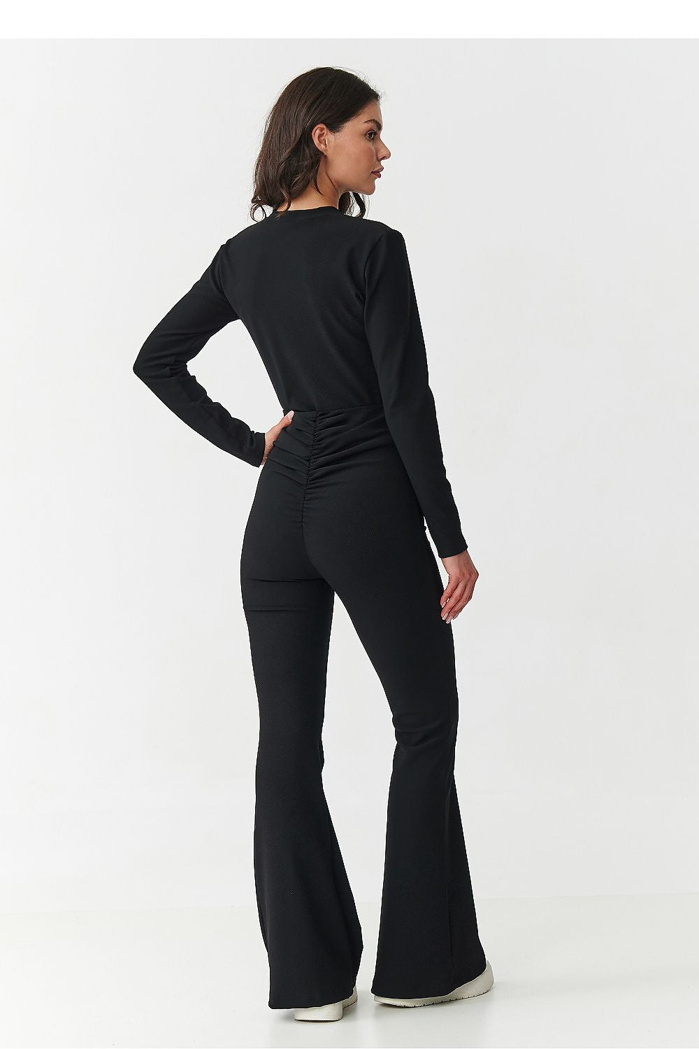 Woman wearing a black long-sleeve top and flared pants on a white background