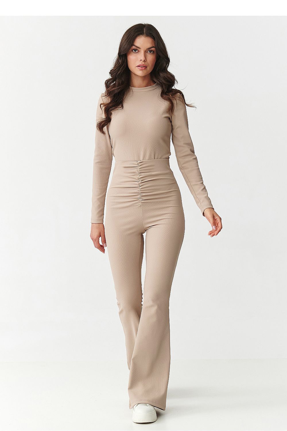 Woman wearing a beige long-sleeve jumpsuit on a white background
