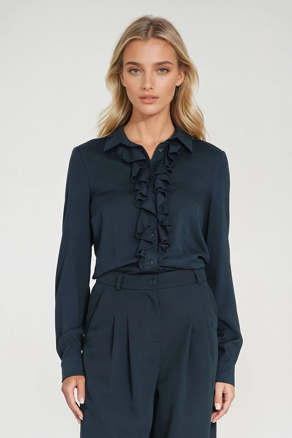 Woman wearing a navy blue blouse with ruffles and matching pants on a white background