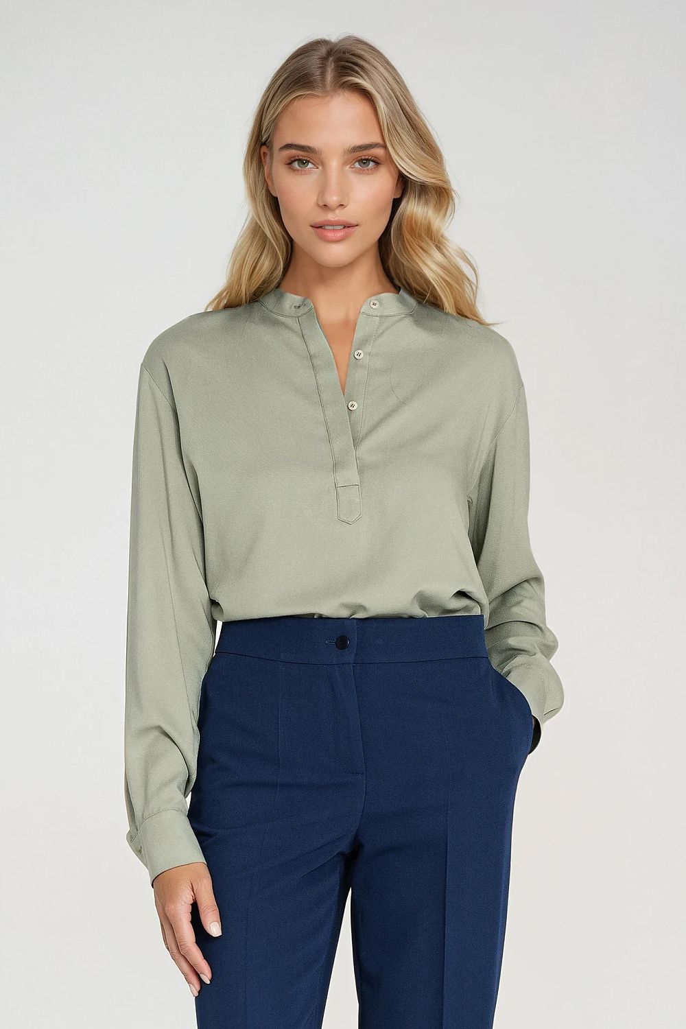 Woman wearing a light green blouse and navy pants on a white background