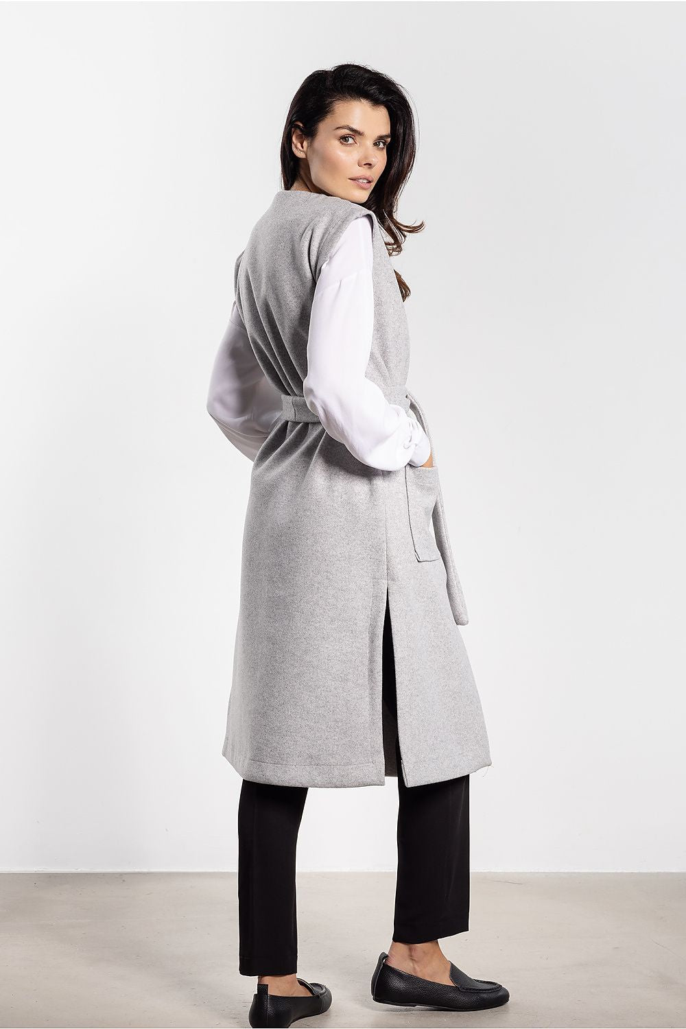 Woman wearing a long gray coat over a white shirt on a white background