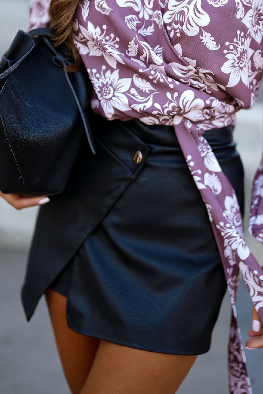 Person wearing a floral blouse and black skirt with a black bag.