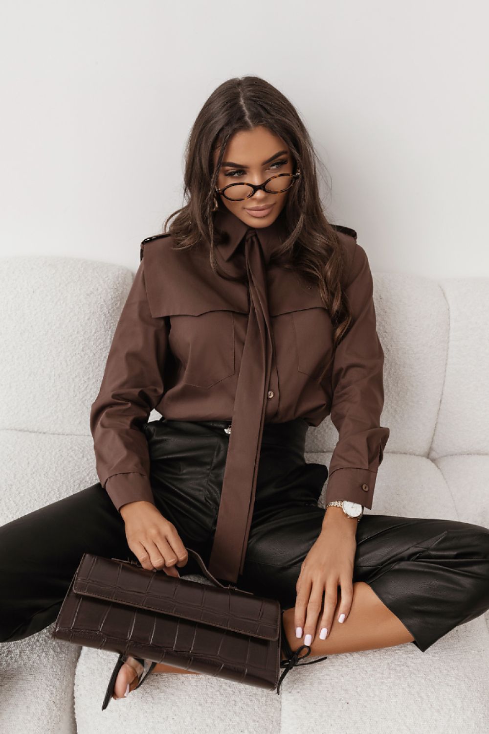Woman in a brown outfit with a matching handbag sitting on a white couch.