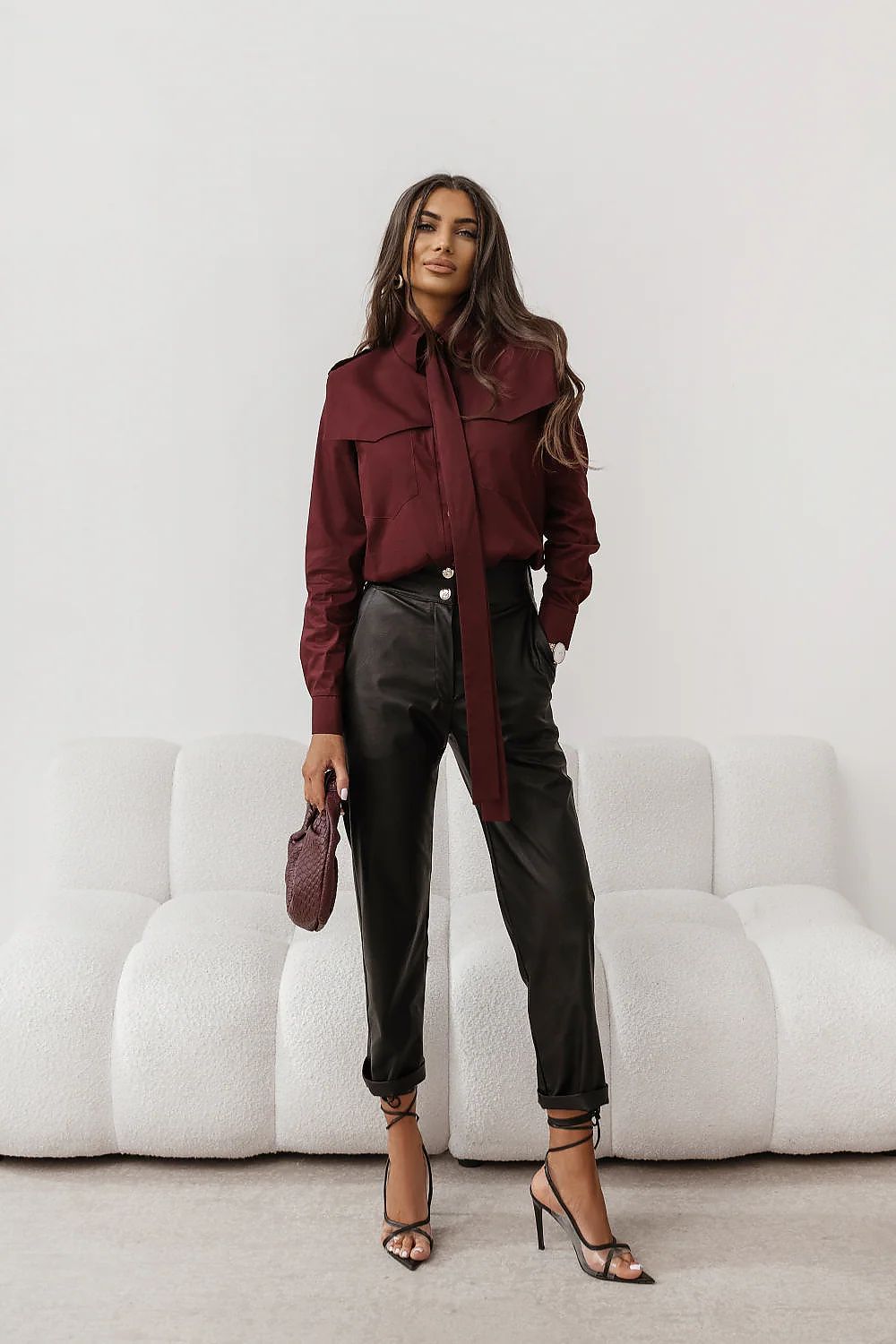 Woman wearing a burgundy coat and black pants in a minimalistic setting