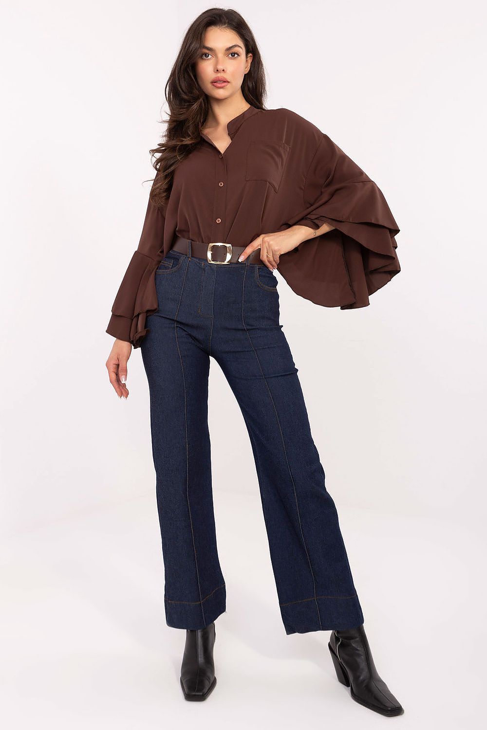 Woman wearing a brown blouse, dark blue jeans, and black boots on a white background
