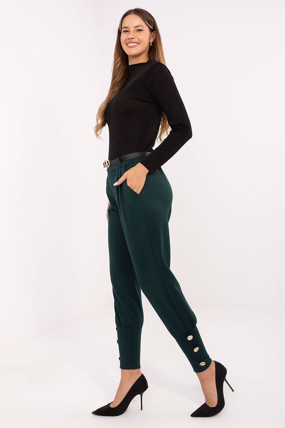 Woman wearing a black top and green pants with button details on a white background