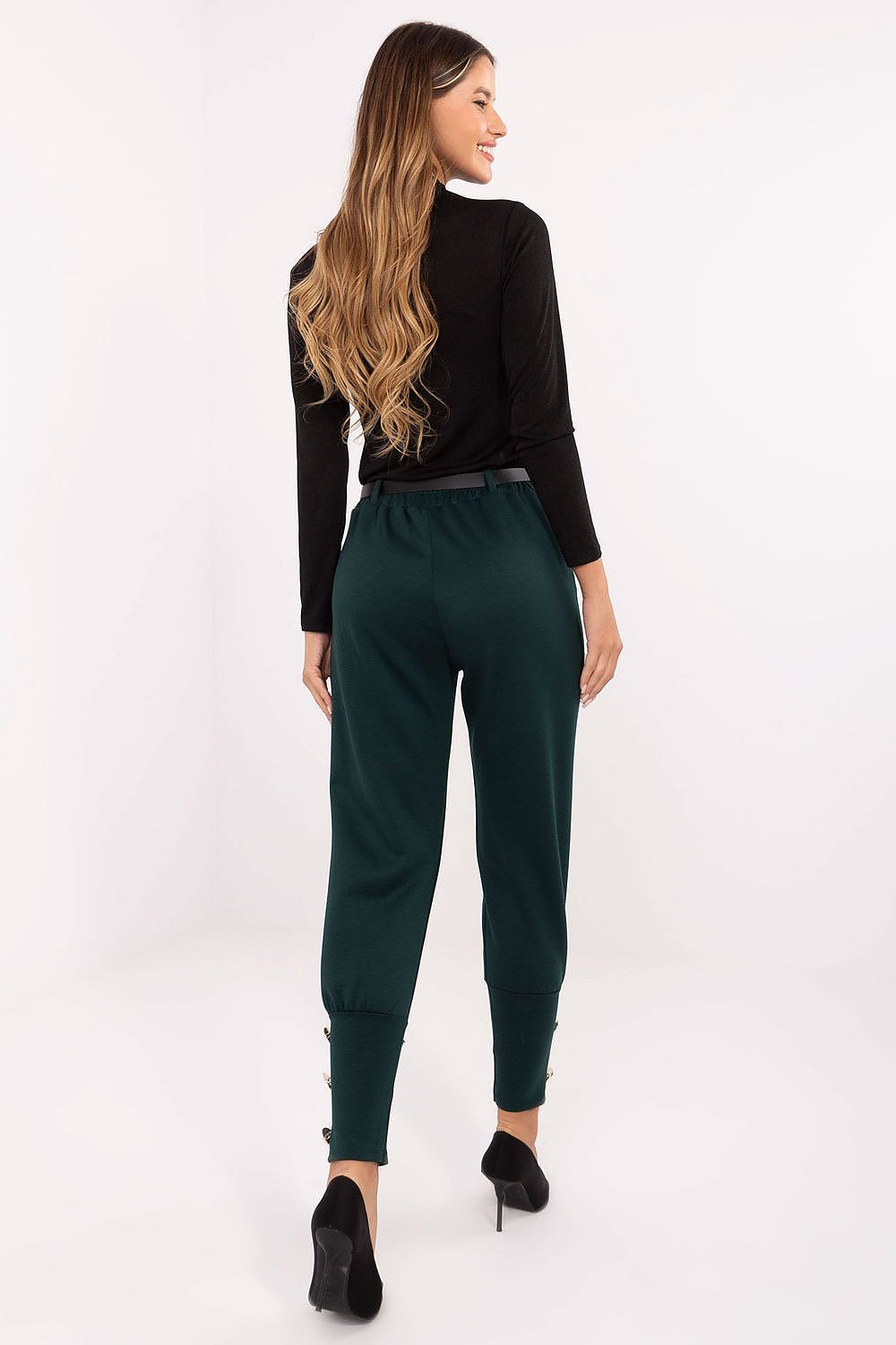 Woman wearing a black top and green pants on a white background