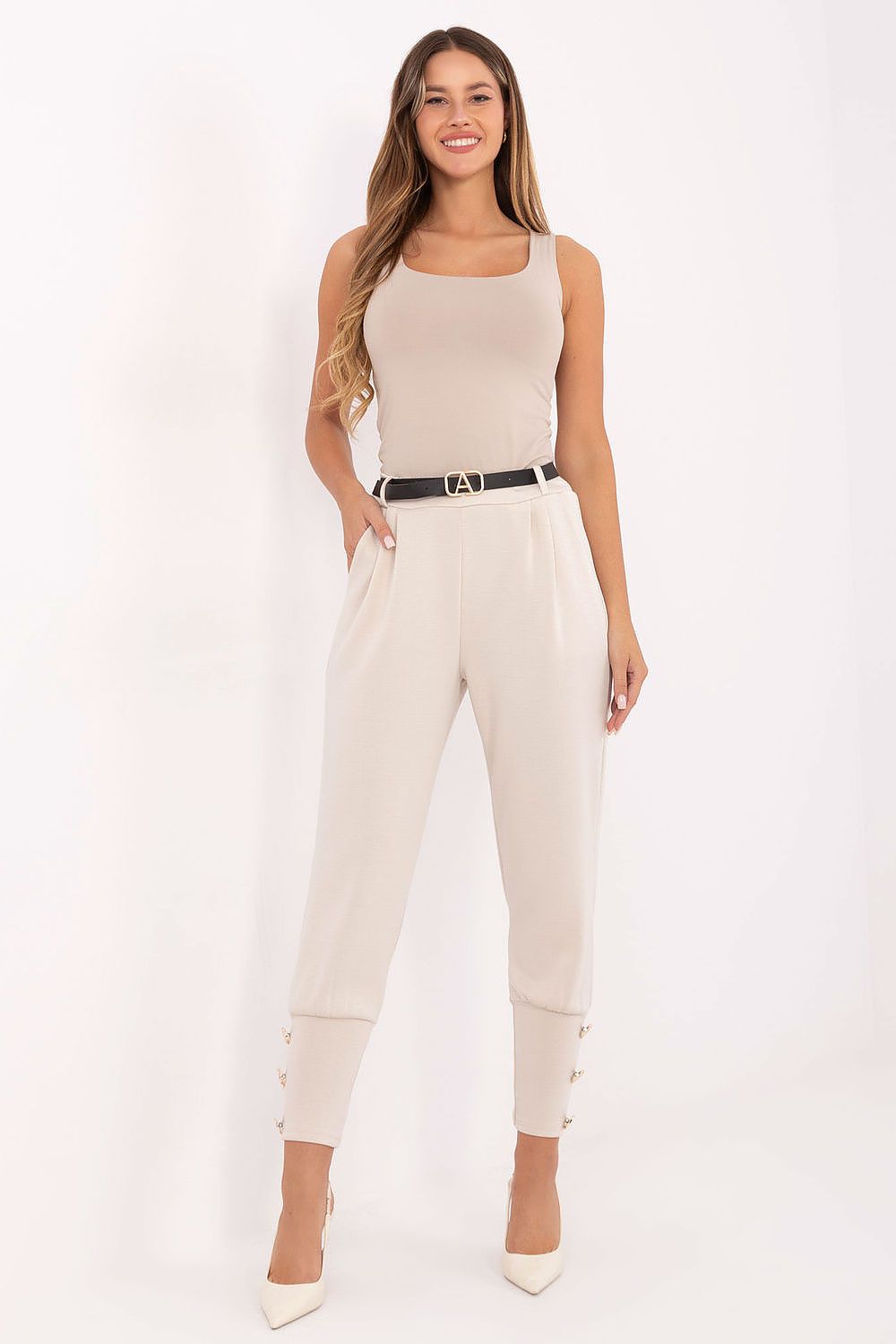 Woman wearing a beige sleeveless top and pants with a belt on a white background