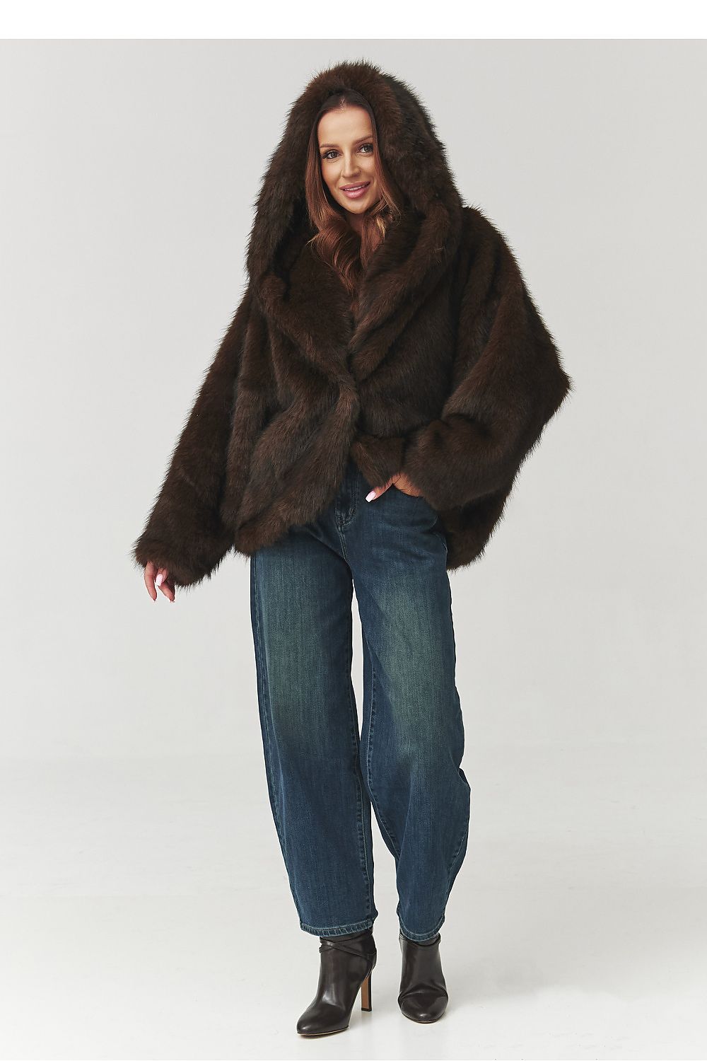 Woman wearing a brown fur coat and blue jeans on a white background