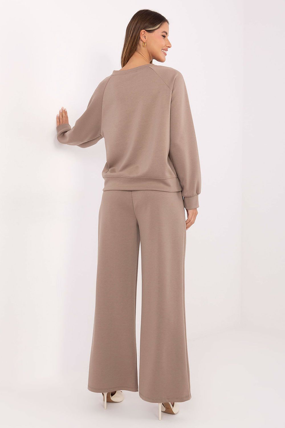 Woman wearing a beige sweater and wide-leg pants against a white background
