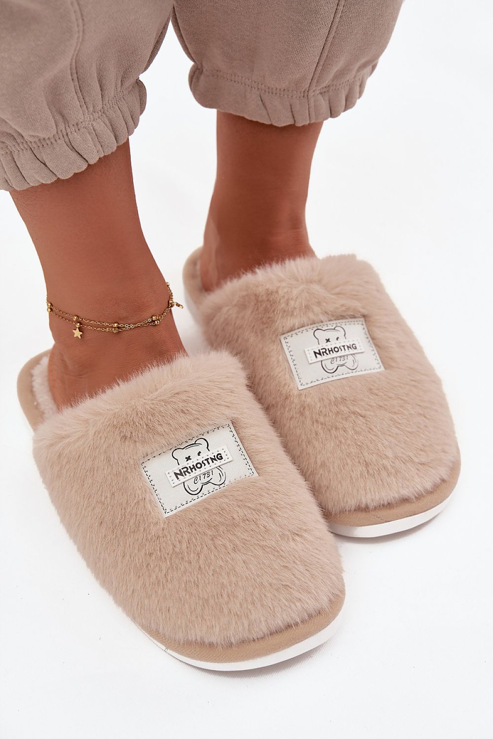 Beige fluffy slippers worn with beige pants on a white background