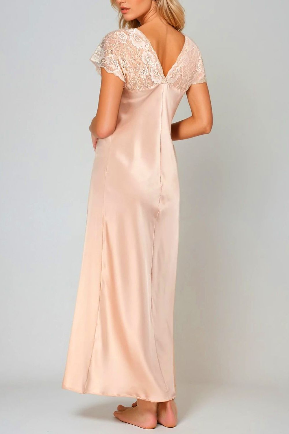 Woman wearing a long, light pink satin nightgown with lace details on a plain background