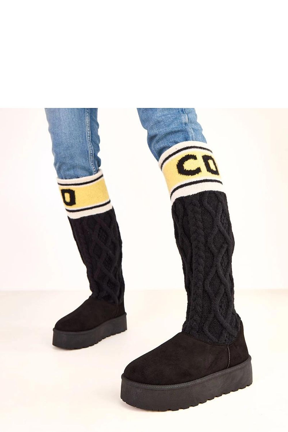 Black knee-high boots with yellow and white accents worn with blue jeans on a light background