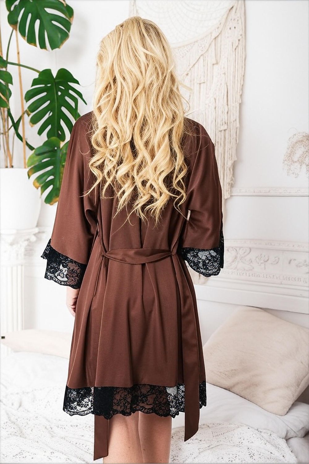 Woman wearing a brown robe with black lace trim in a bedroom setting.