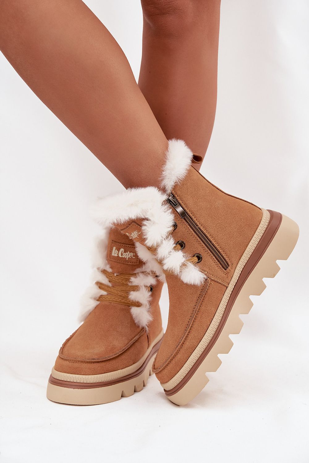 Brown winter boots with white fur trim worn by a person on a light background