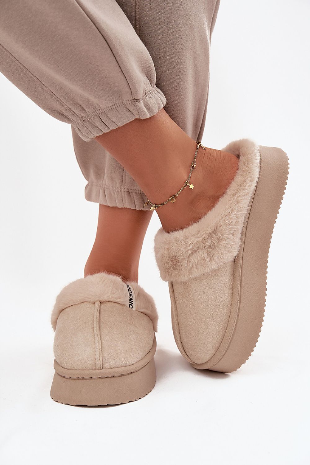 Beige slippers with fuzzy trim worn by a person on a white background