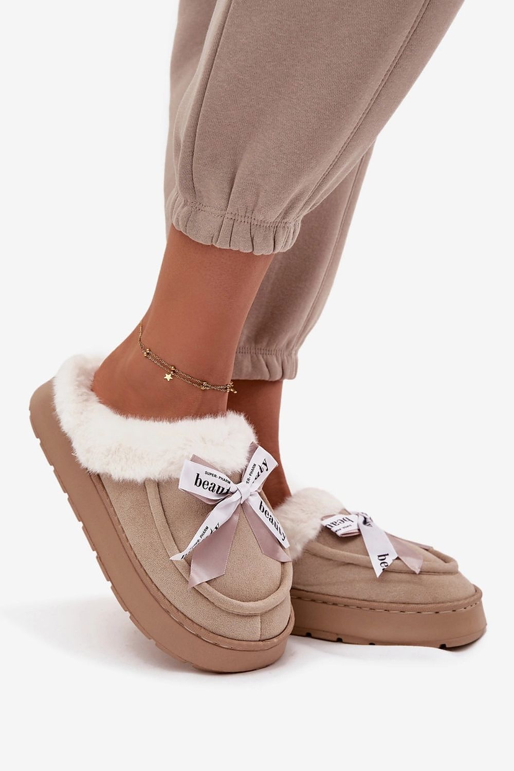 Beige slippers with white fur trim worn by a person on a white background