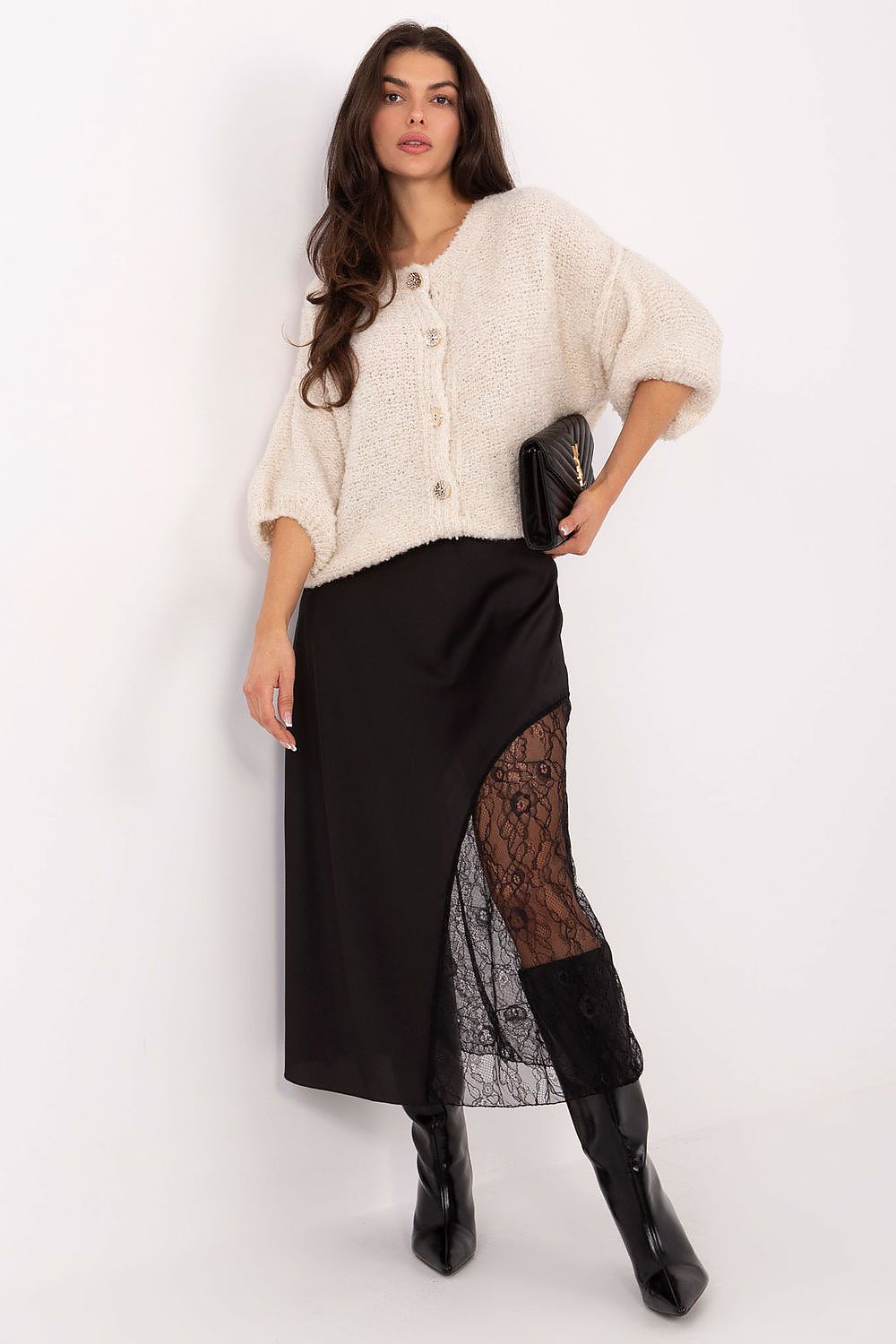 Woman wearing a cream cardigan, black skirt with lace detailing, and black boots on a white background