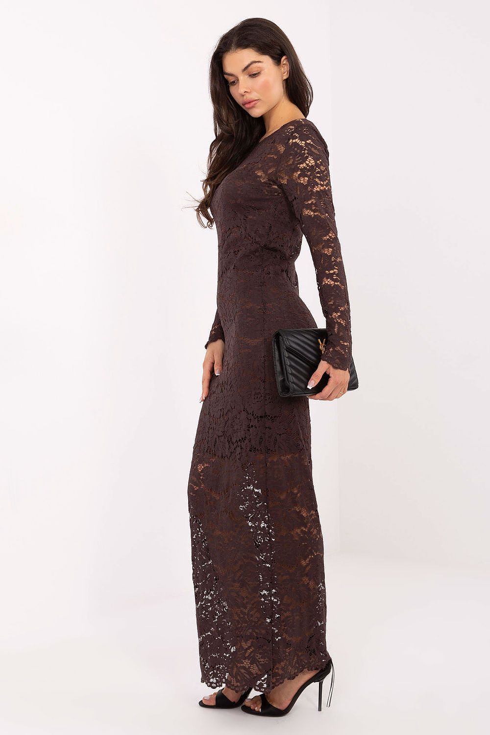 Woman wearing a long brown lace dress holding a black clutch against a white background