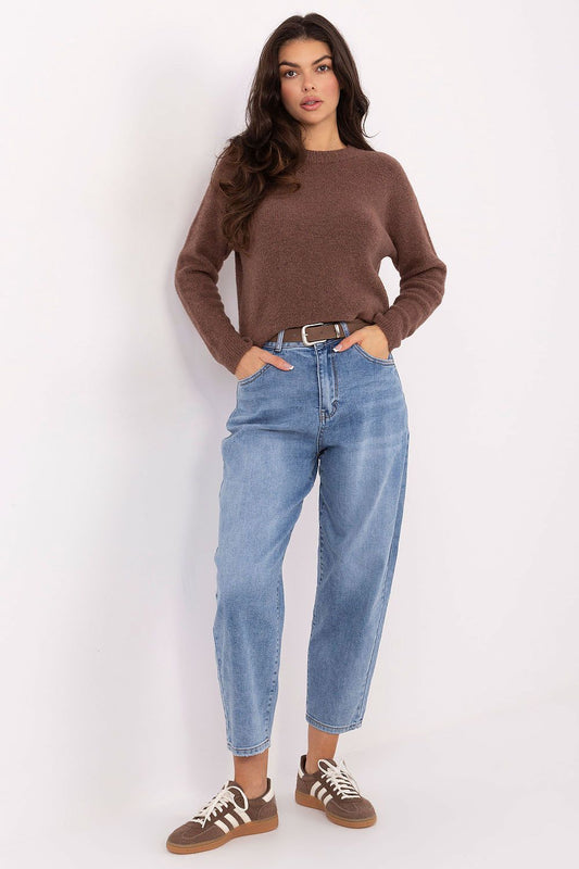 Woman wearing a brown sweater and blue jeans against a white background
