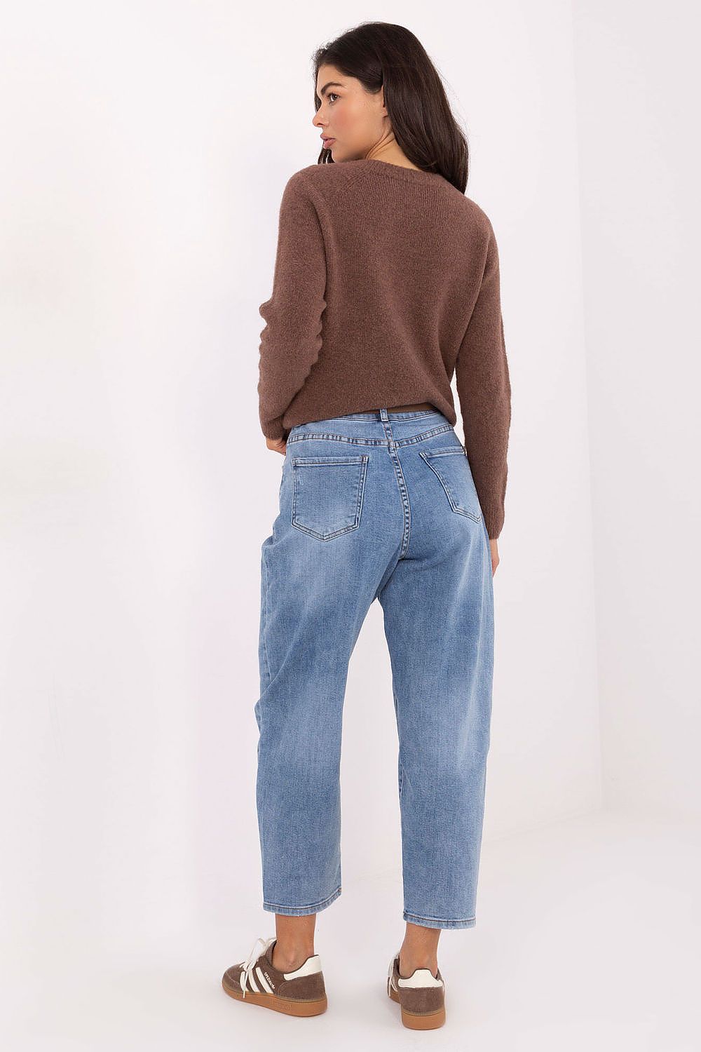 Woman wearing a brown sweater and blue jeans on a white background