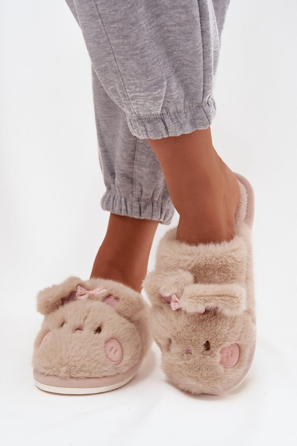 Beige slippers with animal face design worn by a person in gray pants on a white background