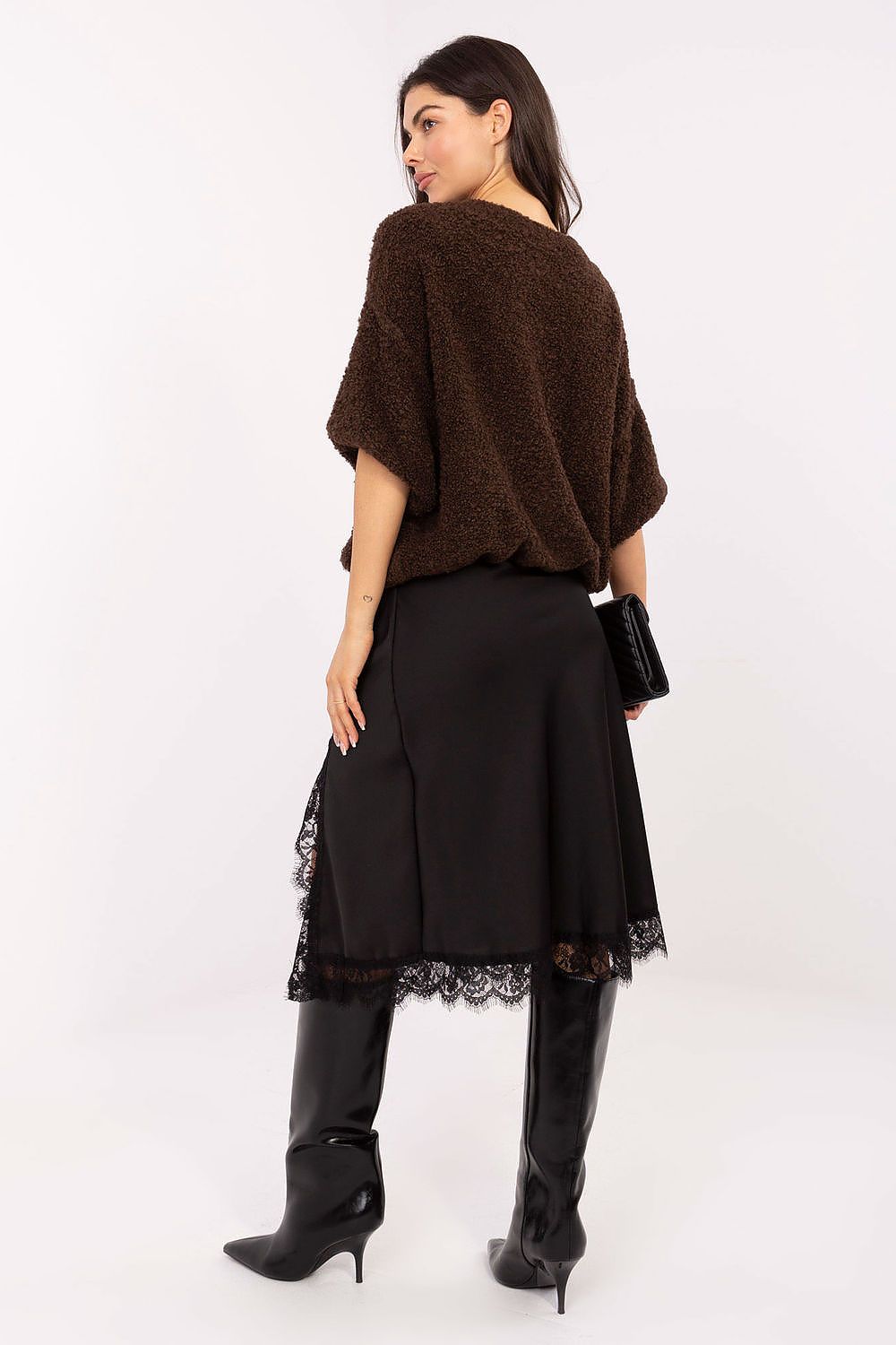 Woman wearing a brown poncho over a black dress with lace details on a white background