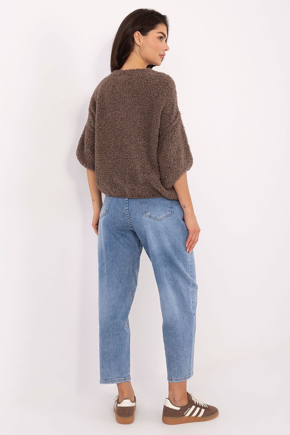 Woman wearing a brown sweater and blue jeans against a white background