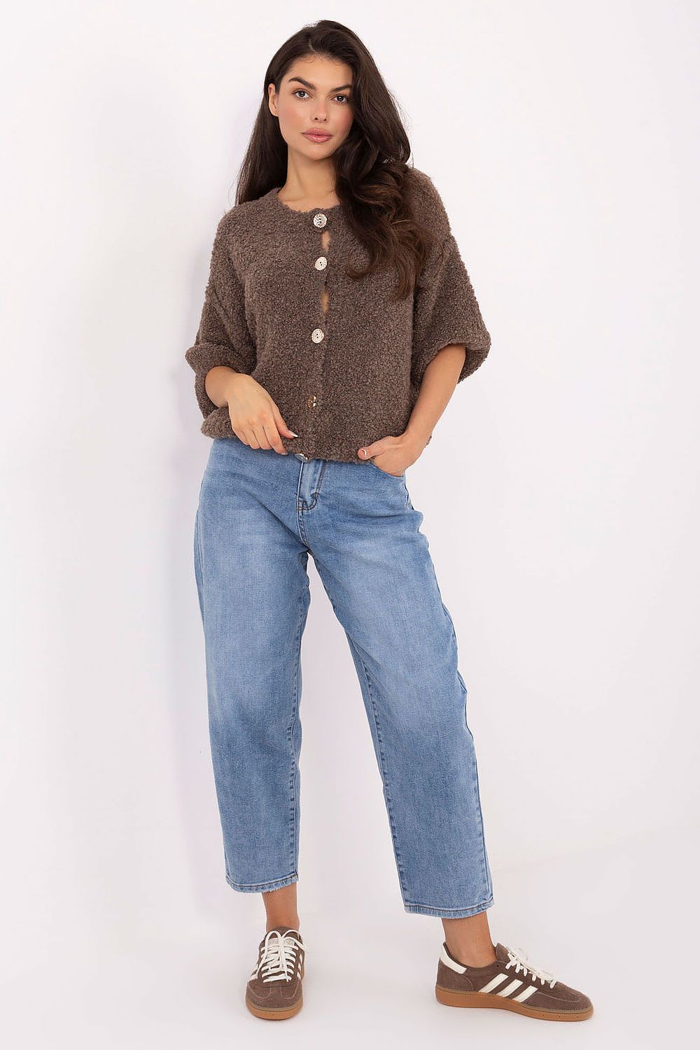Woman wearing a brown cardigan, blue jeans, and brown shoes on a white background