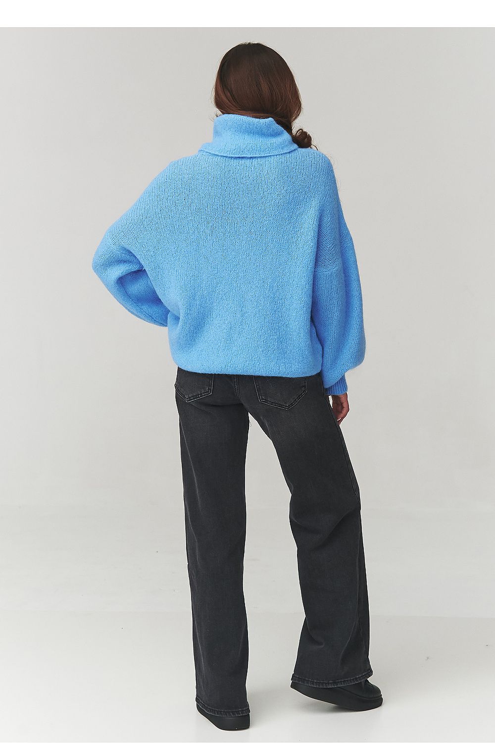 Person wearing a blue sweater and black pants on a white background