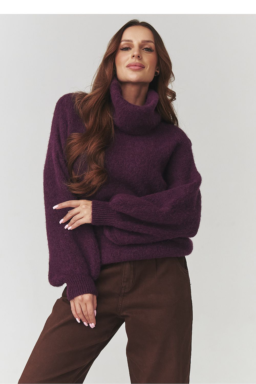 Woman wearing a purple sweater and brown pants against a white background
