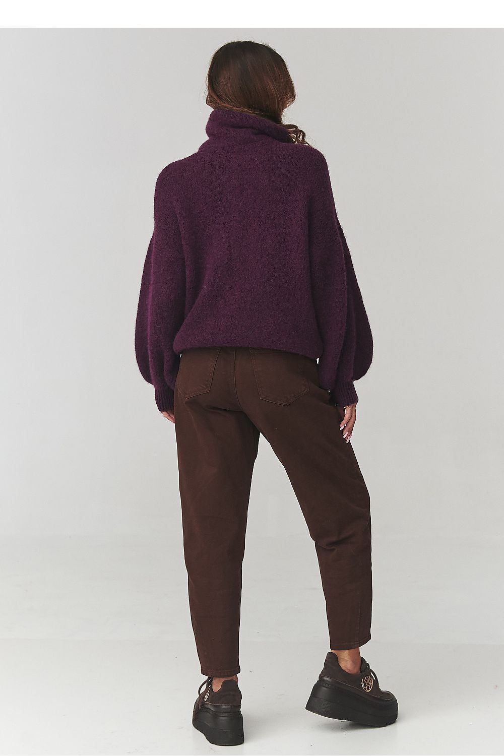 Person wearing a purple sweater and brown pants on a white background
