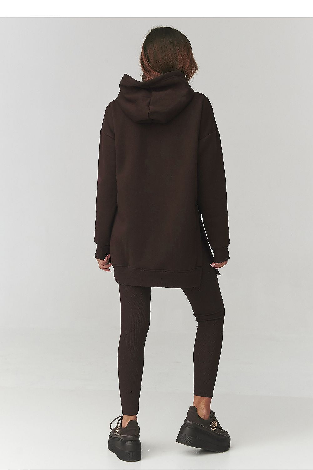 Person wearing a long brown hoodie and leggings on a white background