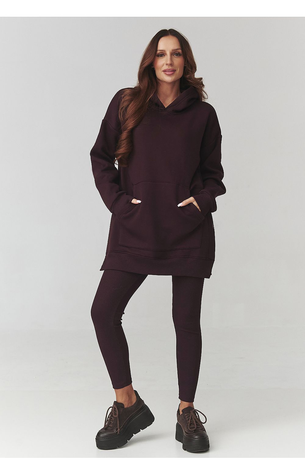 Woman wearing a dark brown hoodie and leggings on a white background