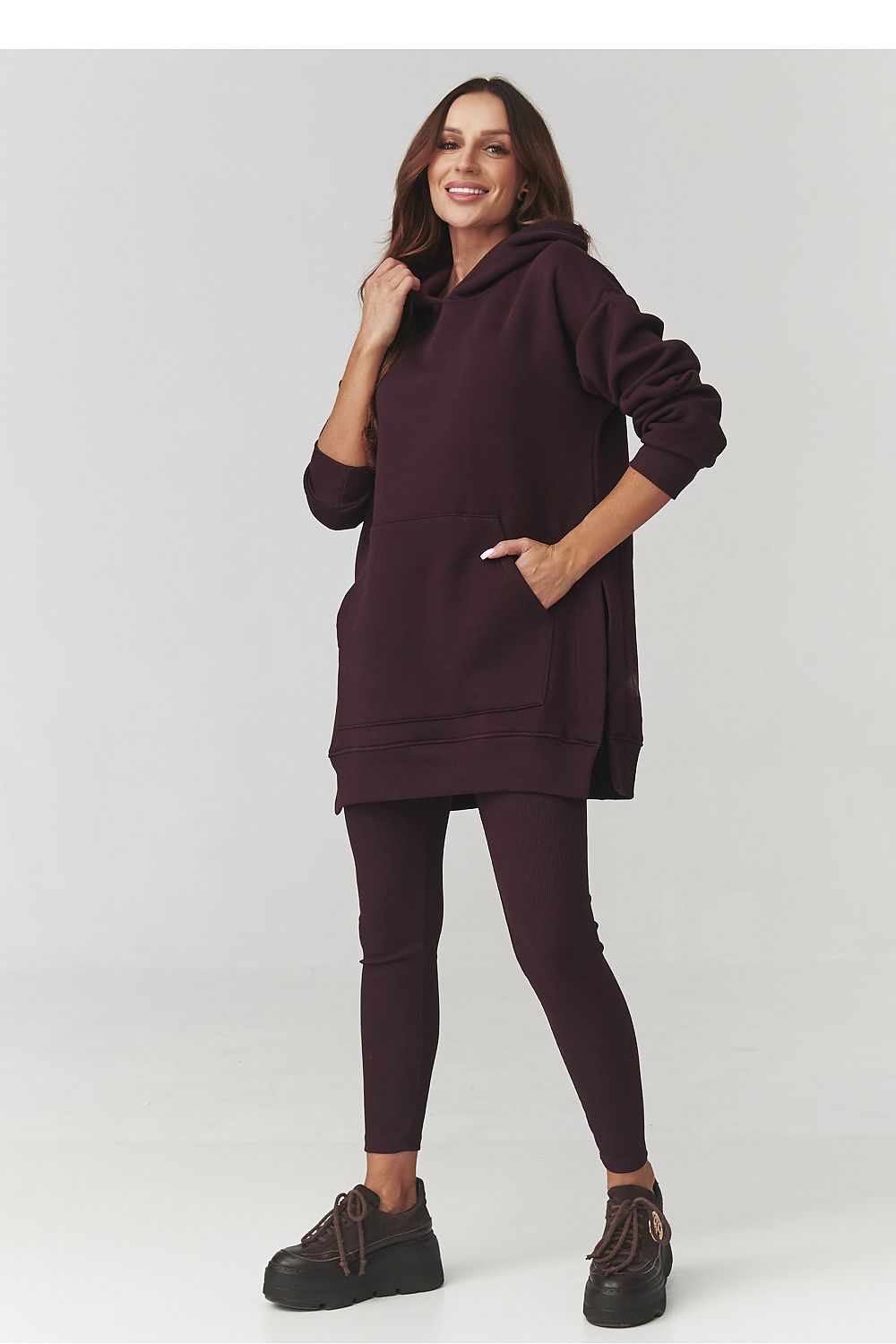 Woman wearing a dark brown hoodie and leggings on a white background
