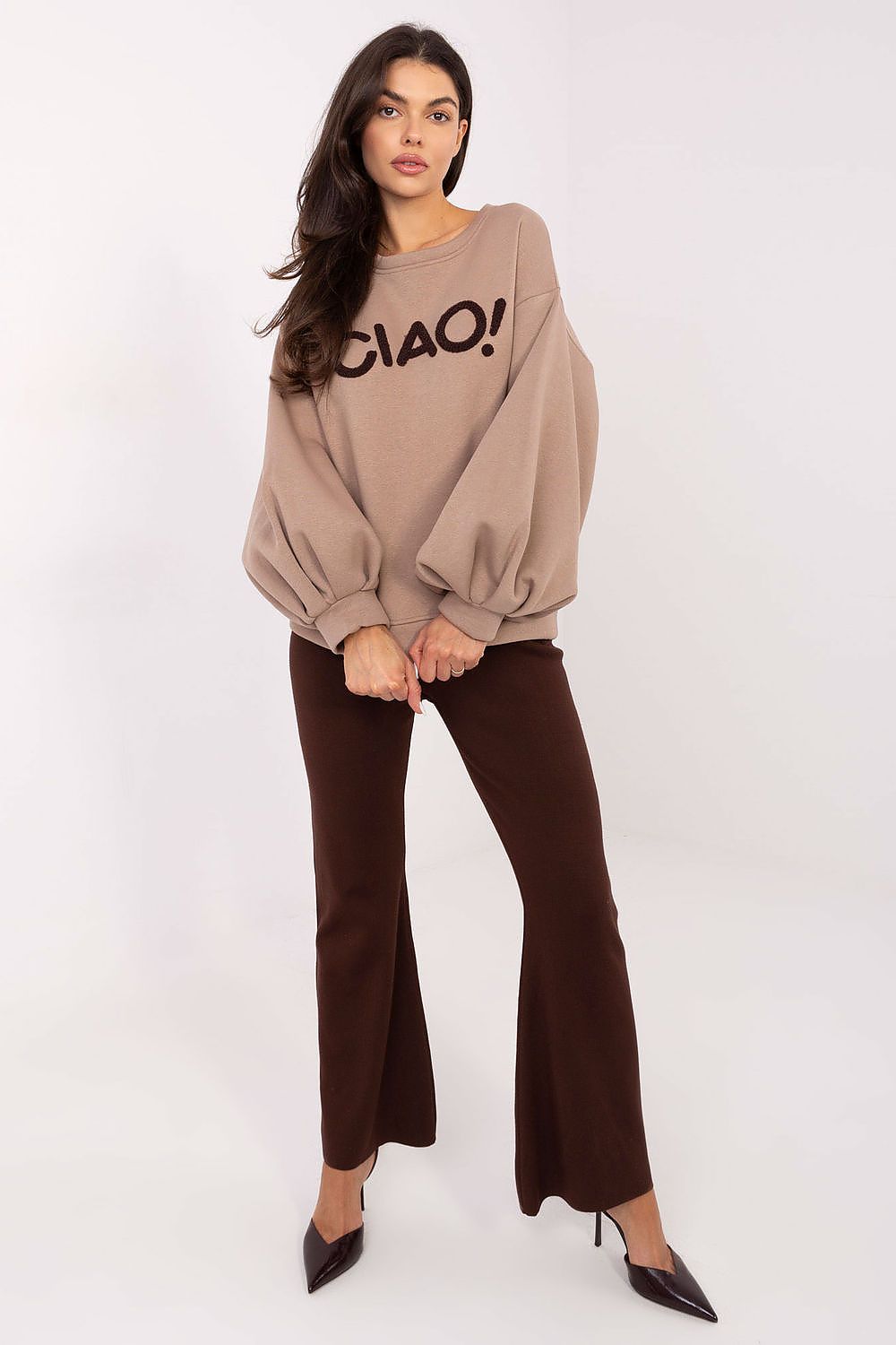 Woman wearing a beige sweater with 'CIAO!' text and brown pants on a white background