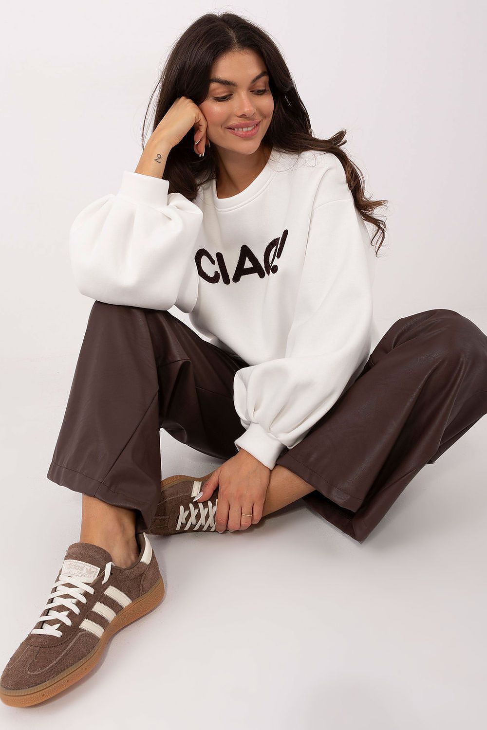 Woman wearing a white sweatshirt with 'CLAI' text, brown pants, and brown sneakers on a white background