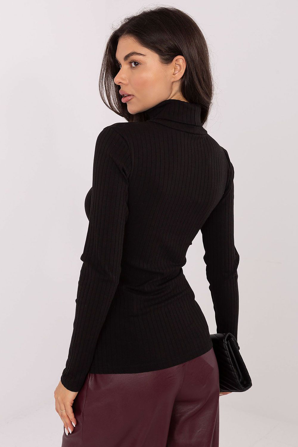 Woman wearing a black turtleneck sweater and maroon pants against a white background