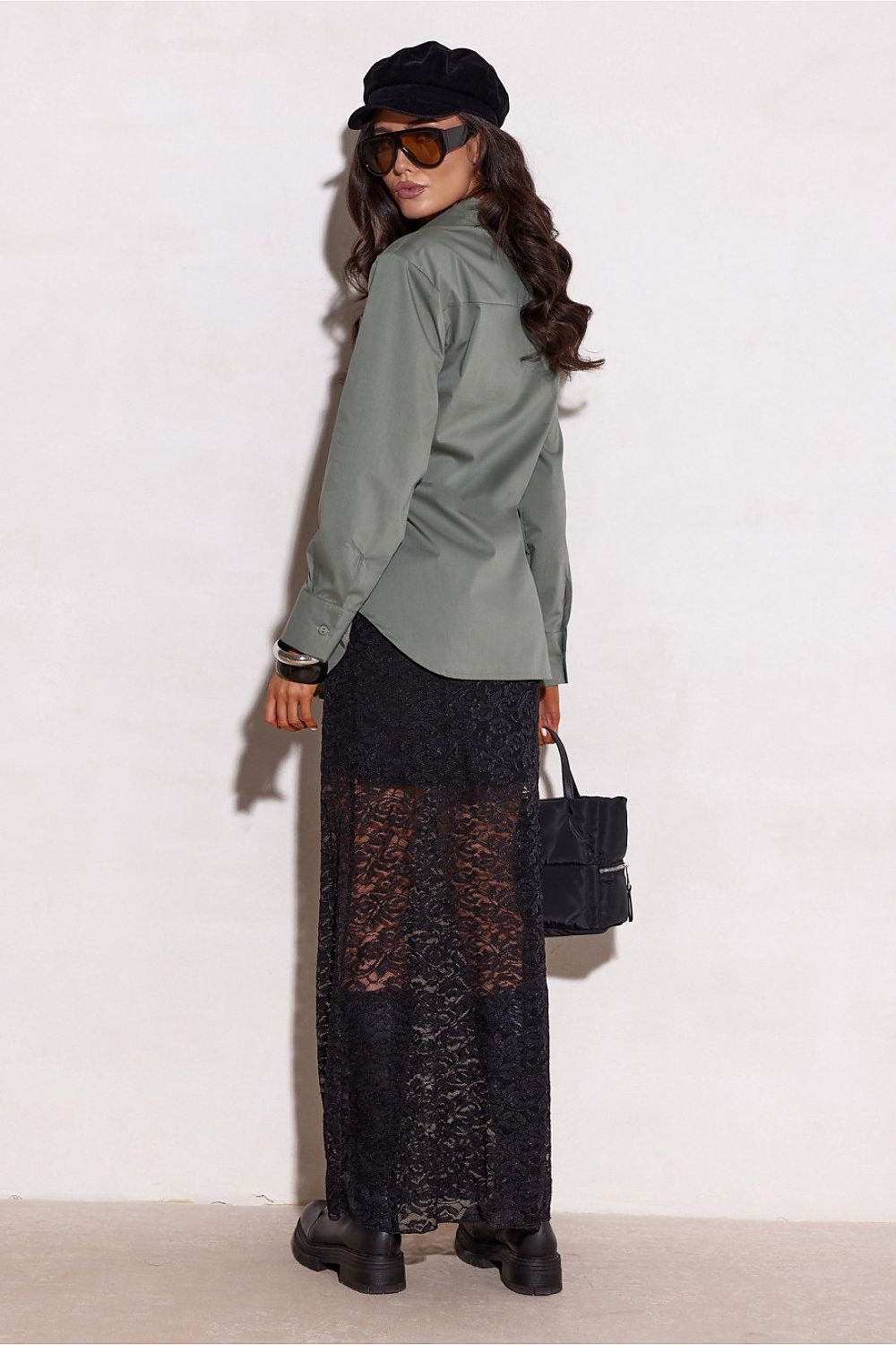 Woman wearing a green shirt, black cap, sunglasses, and black lace dress against a white background