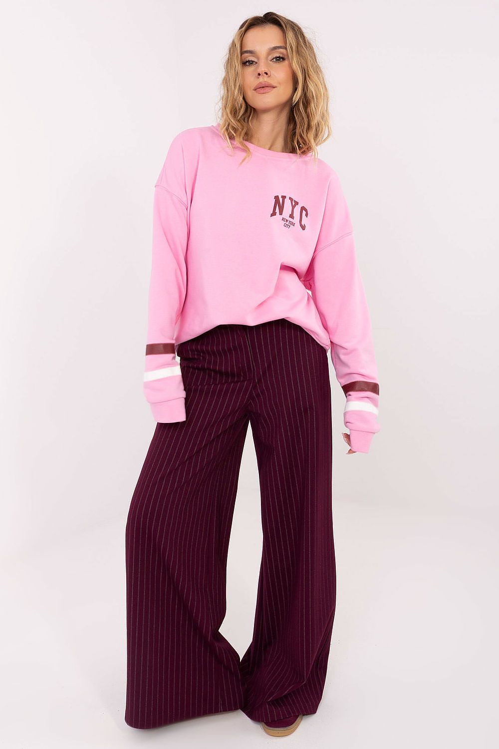 Person wearing a pink 'NYC' sweatshirt and purple pants on a white background