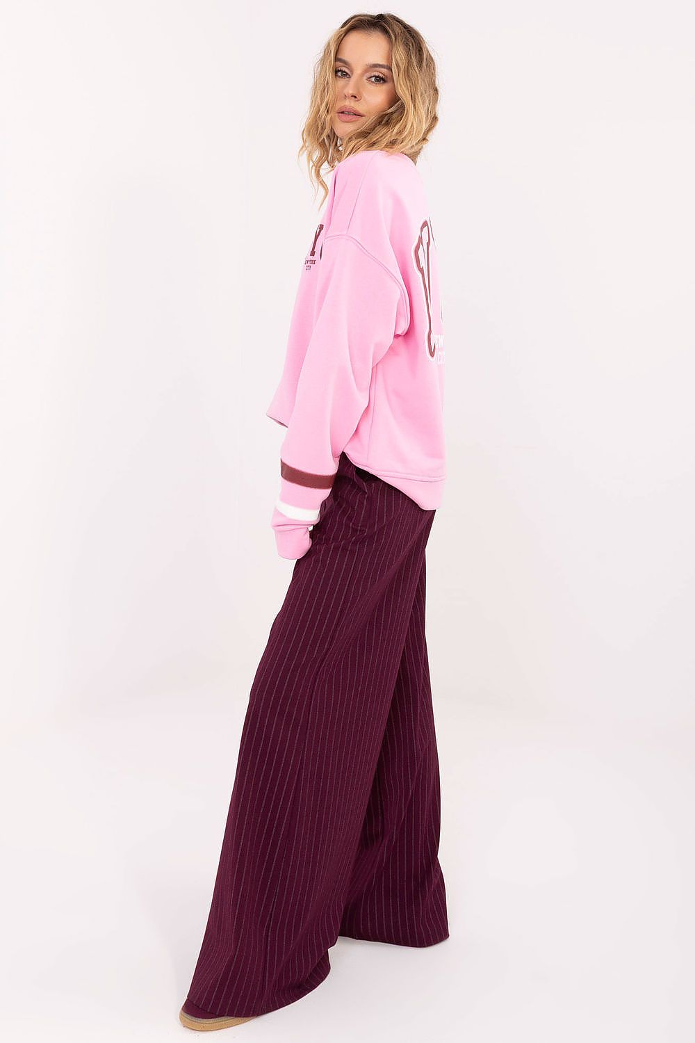 Person wearing a pink sweatshirt and purple pants on a white background