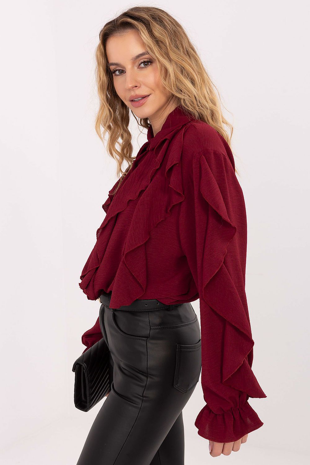 Woman wearing a burgundy ruffled blouse with black pants on a white background