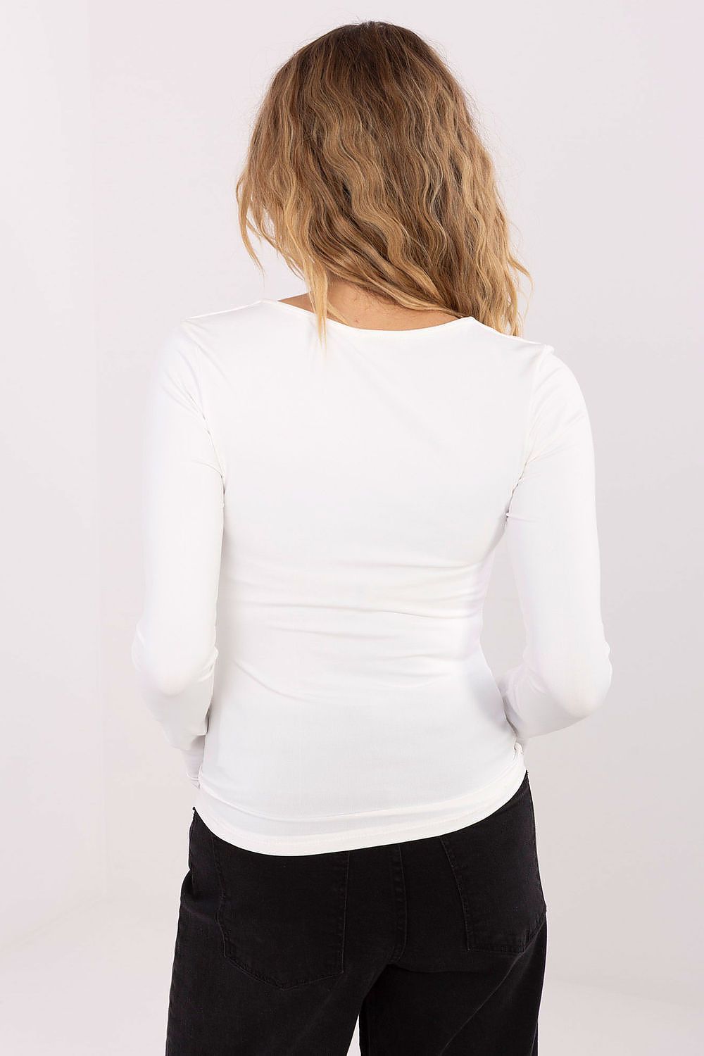 Person wearing a white long-sleeve top and black pants on a plain background