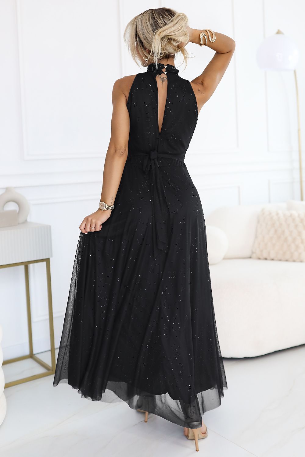Woman wearing a black halter neck dress in a minimalistic room.