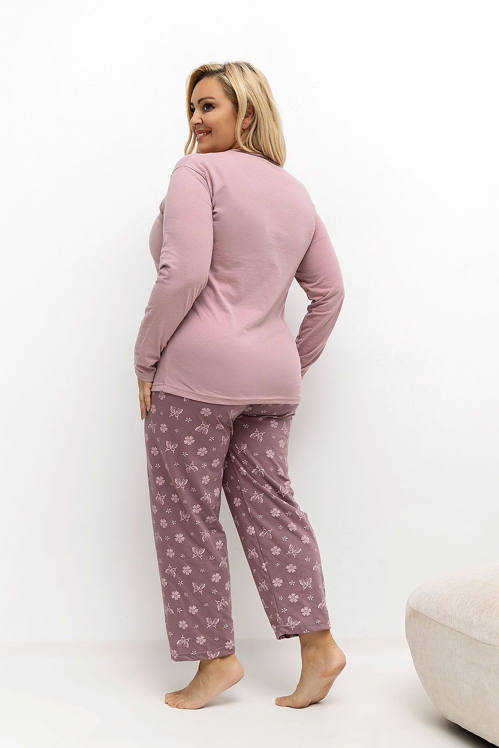Woman wearing a pink long-sleeve top and patterned pants on a white background