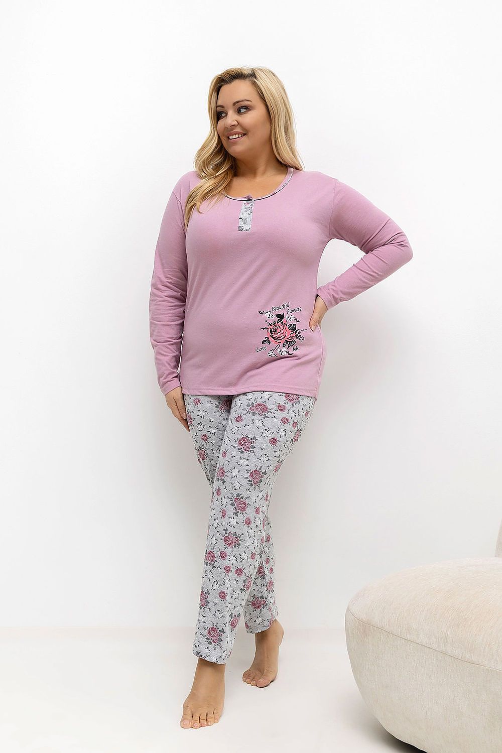 Woman wearing a pink long-sleeve top and floral pants on a white background
